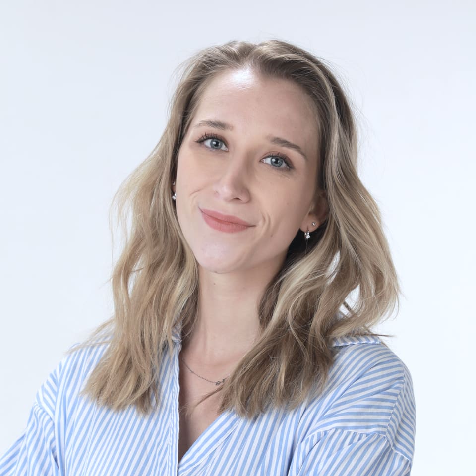 Anna lächelt in einem blau-weiß gestreiften Hemd vor hellem Hintergrund