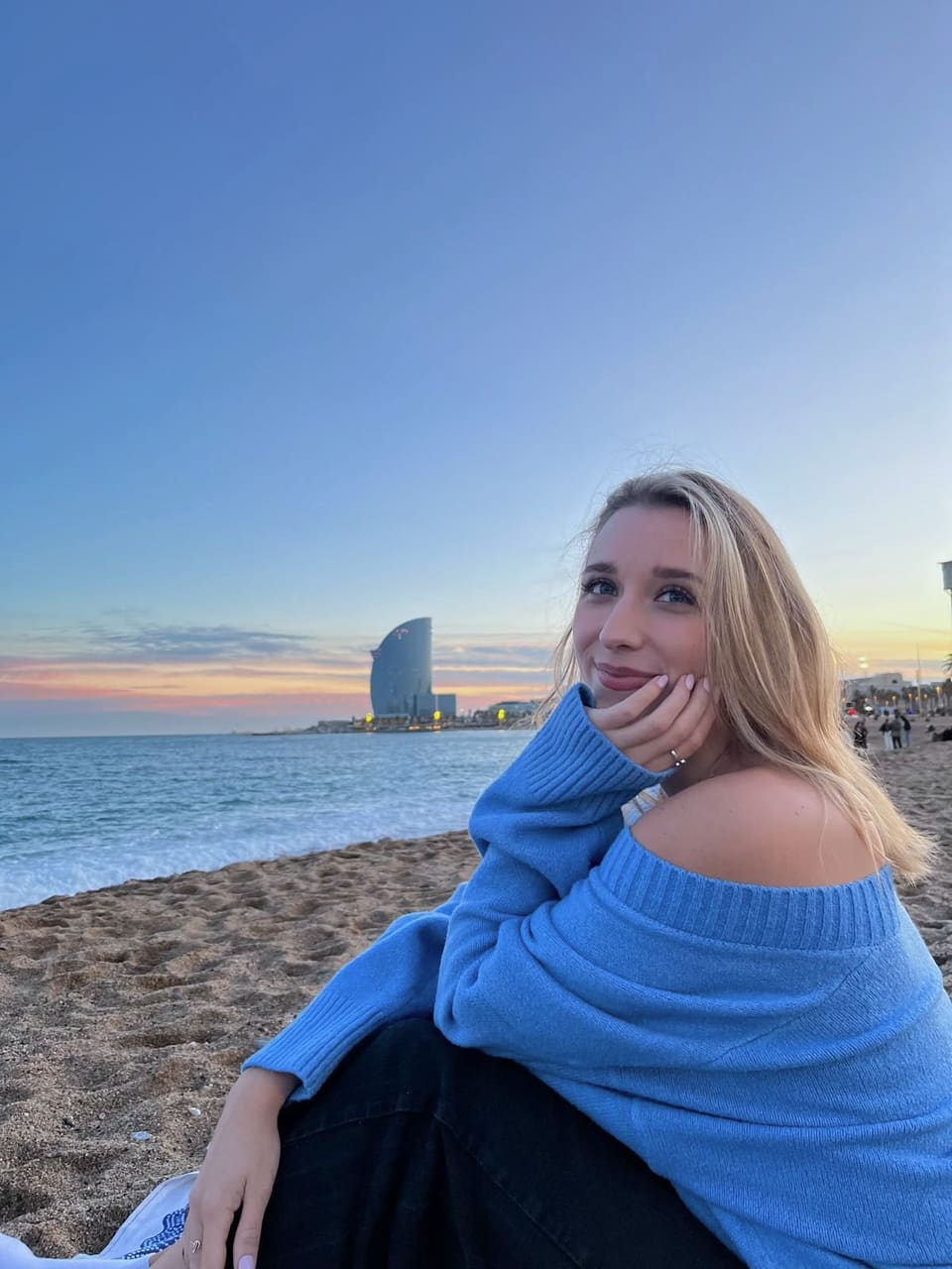 Anna in einem hellen Kleid, allein an einem Strand in Barcelona bei Sonnenuntergang