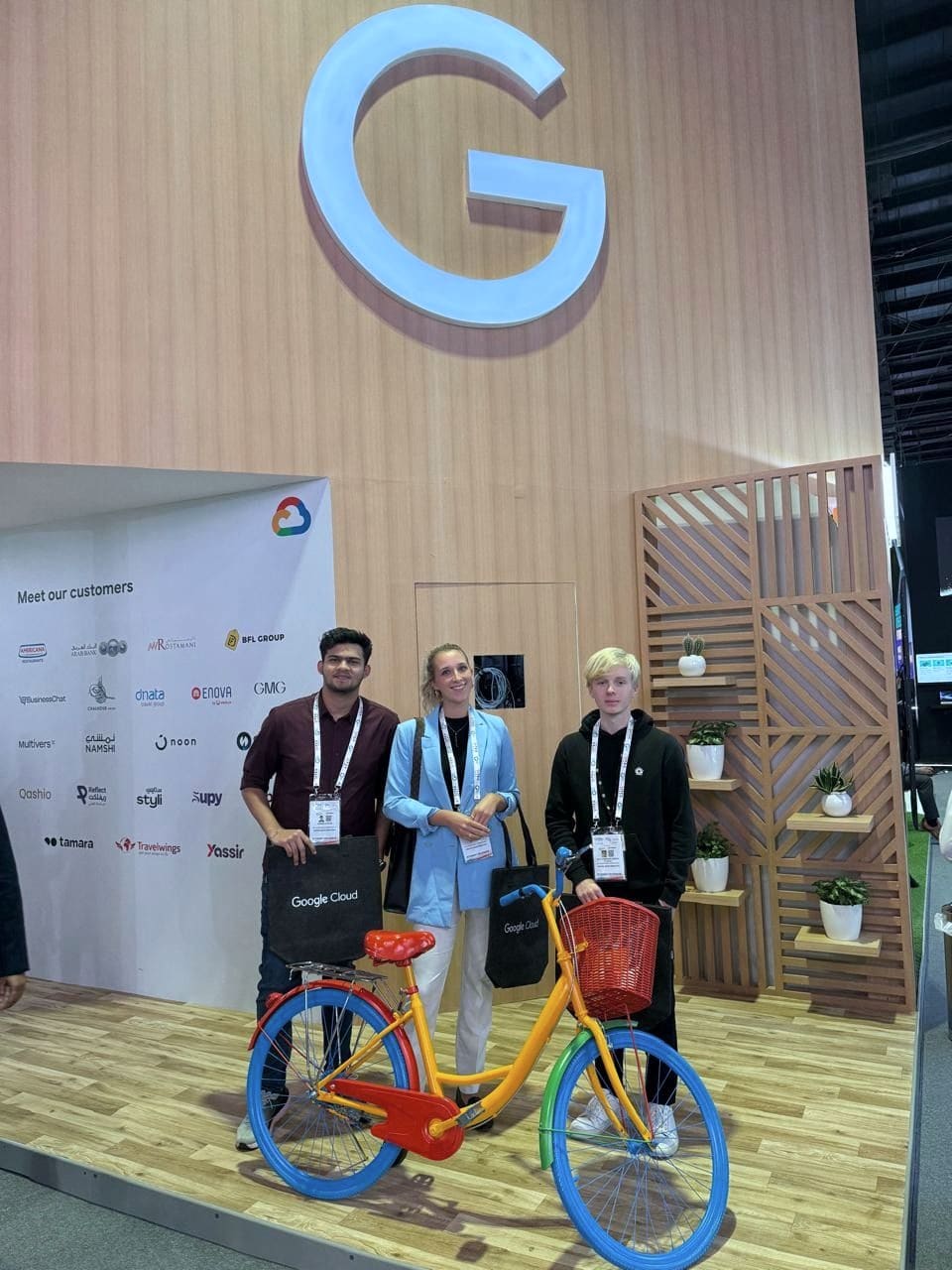 Anna in blauem Blazer mit zwei weiteren Personen an einem Messestand, neben einem bunten Fahrrad