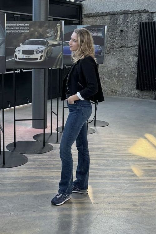 Anna in schwarzer Jacke und Jeans betrachtet in einer Halle mit Glasdach große Bentley-Fototafeln