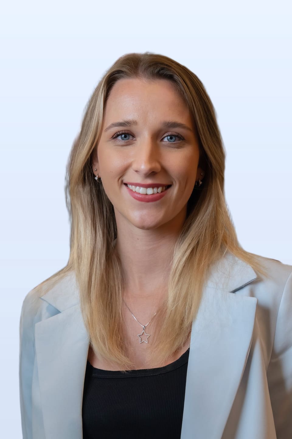 Anna mit breitem Lächeln in einem hellen graublauen Blazer und schwarzem Oberteil vor einem schlichten hellen Hintergrund