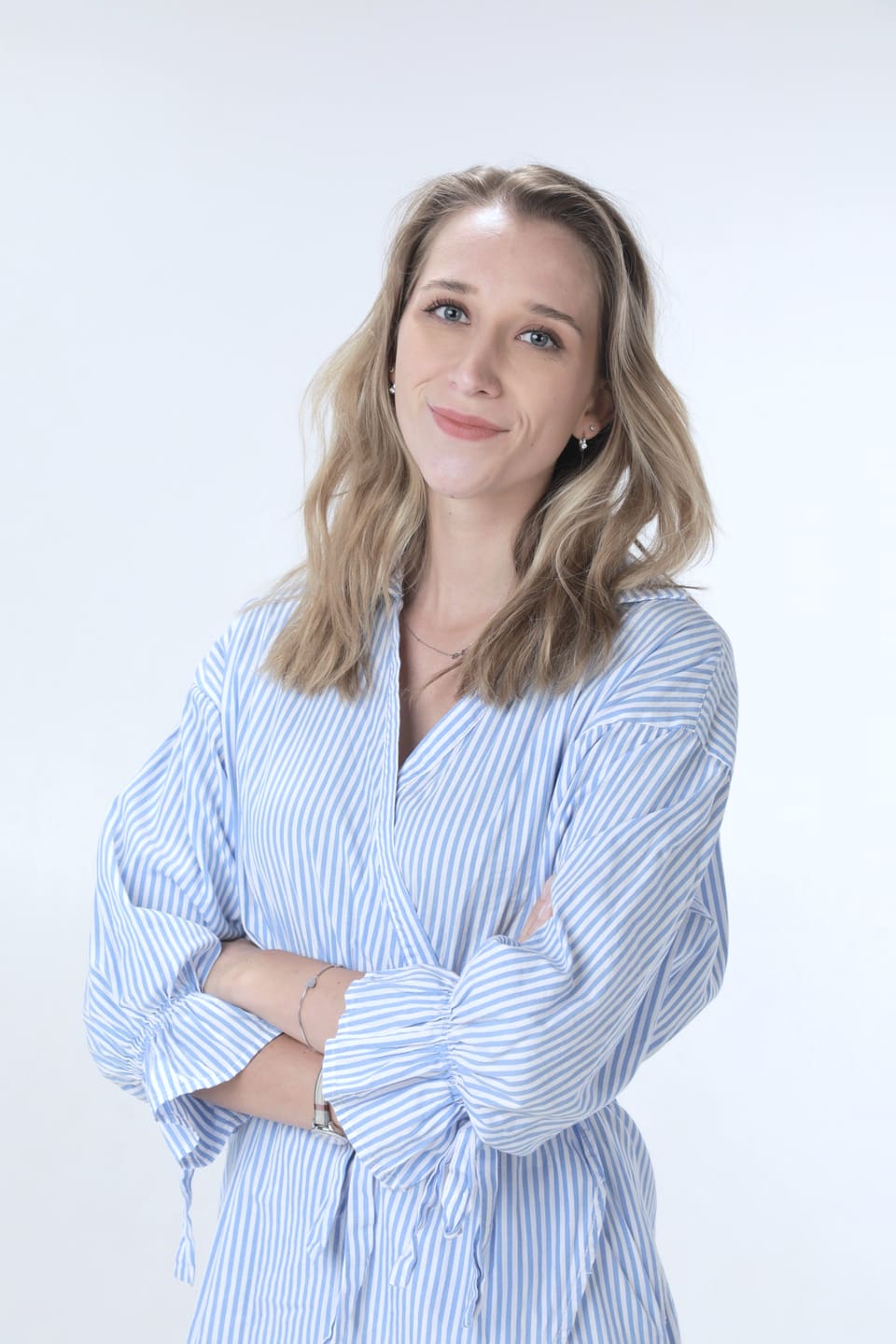 Anna in a blue shirt, smiling, in front of a light background
